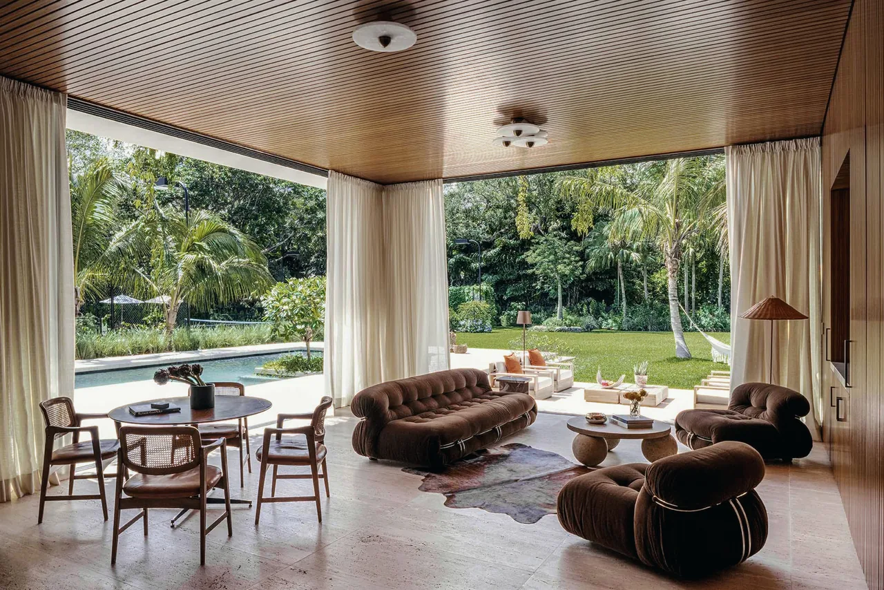 Open living room and dining area with wood ceiling and large windows opening to a landscaped garden and pool at Angel Oaks project.