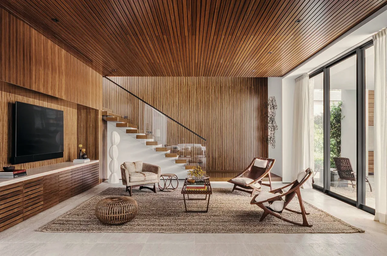 Living area featuring vertical wood paneling, floating staircase, woven rug, and floor-to-ceiling glass doors.