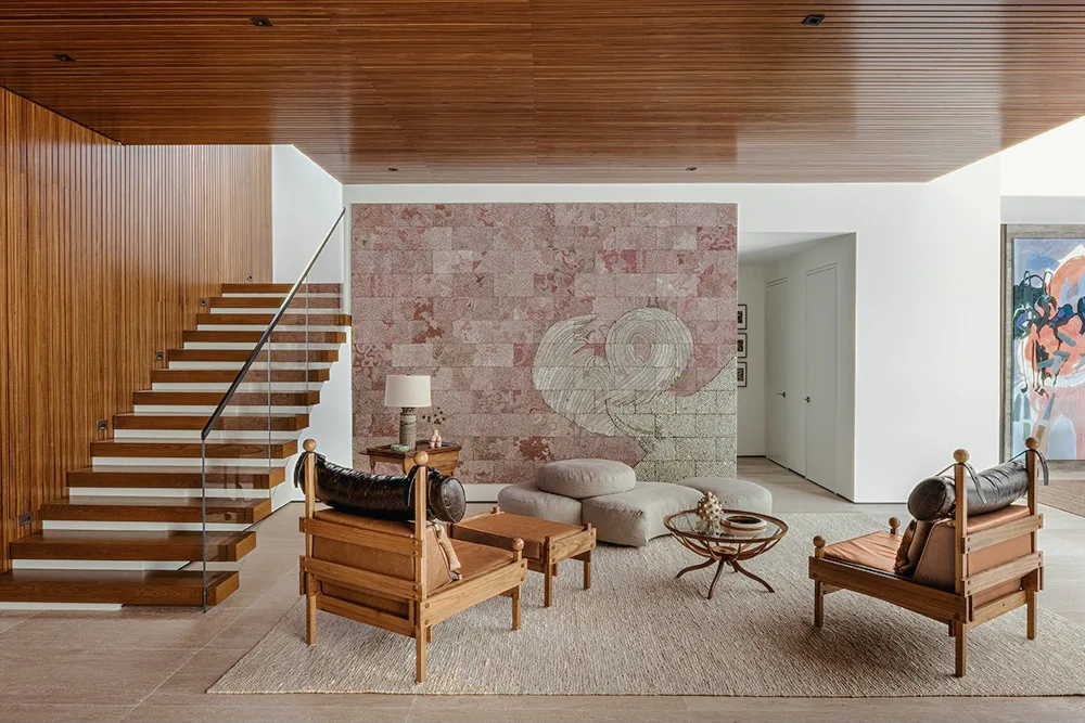 Living room with floating wood stairs, wooden paneled ceiling and wall, neutral furnishings, and textured stone feature wall.