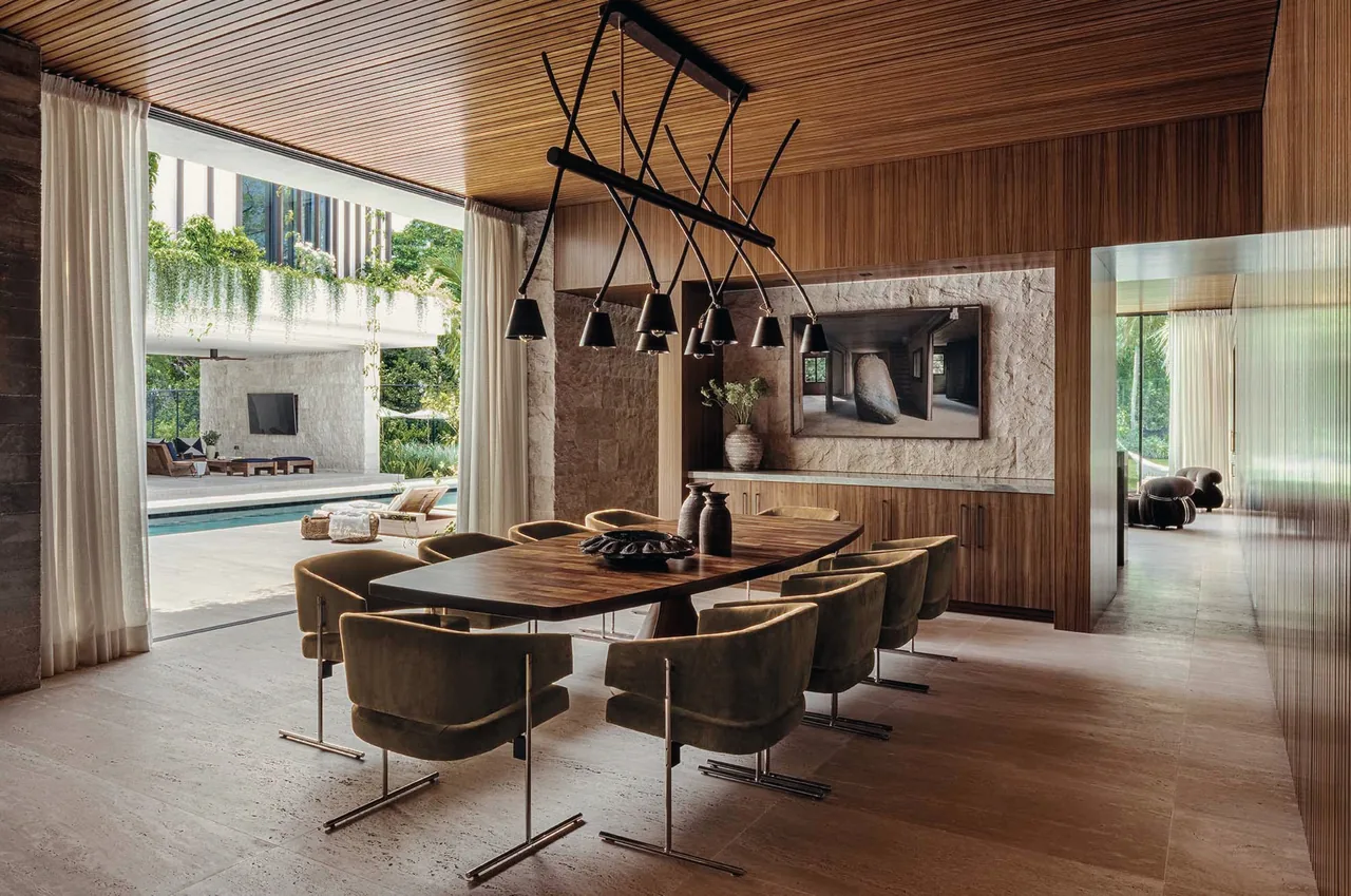 Dining area features a wood-paneled ceiling, textured stone wall, and black pendant lighting, opening to a pool courtyard.