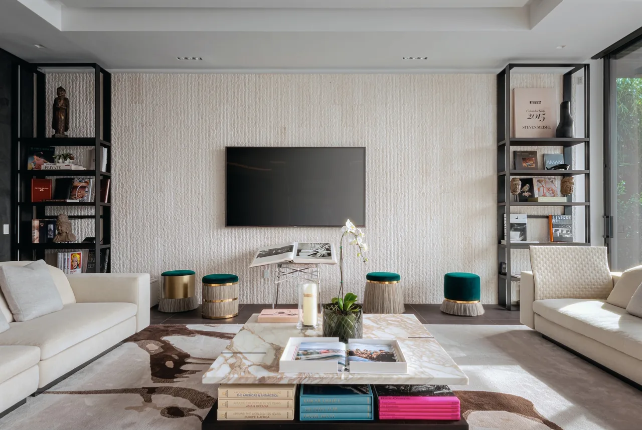 Living room of the Net Zero House features neutral sofas, a wall-mounted TV, and built-in shelving with artistic decor and books.