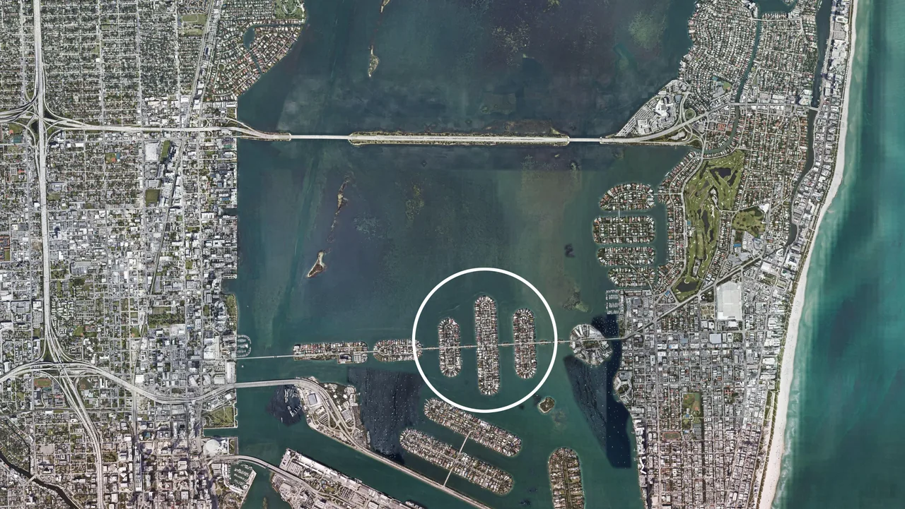 Satellite aerial view showing three elongated man-made islands in water off a city coast with urban grid layout.
