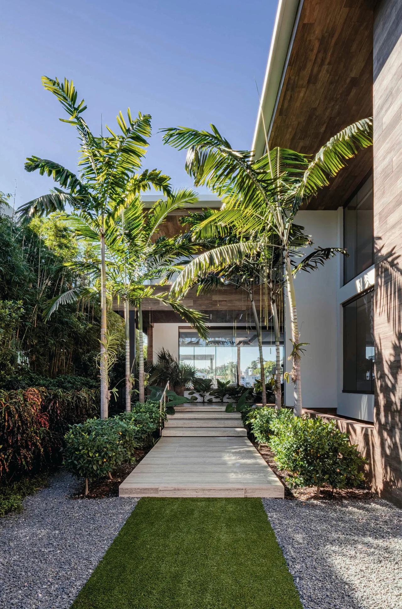The house features a pathway with surrounding greenery leading to an entrance with glass doors.