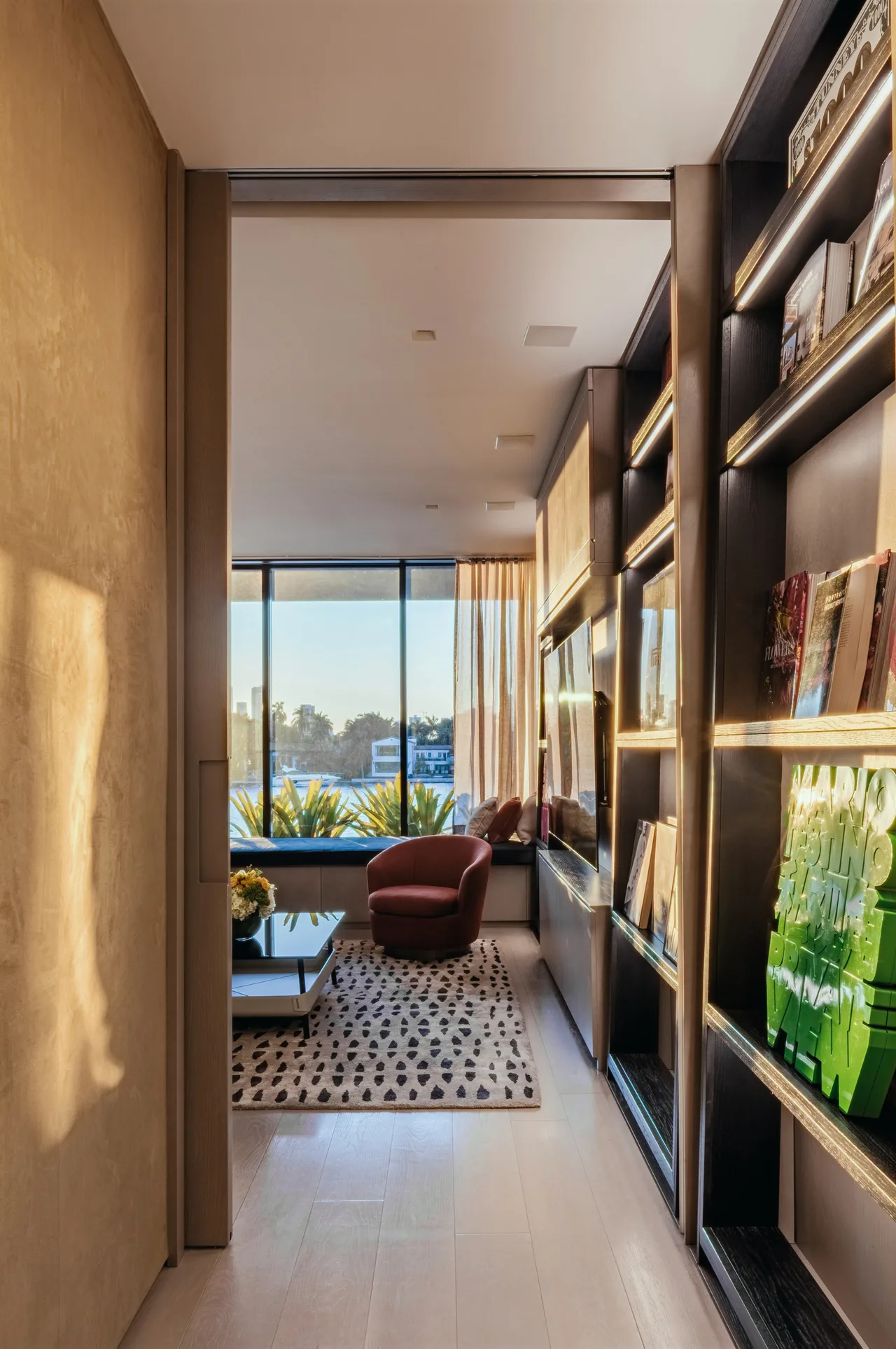 Modern living room with floor-to-ceiling glazing, built-in shelving, and a patterned rug by a large window.