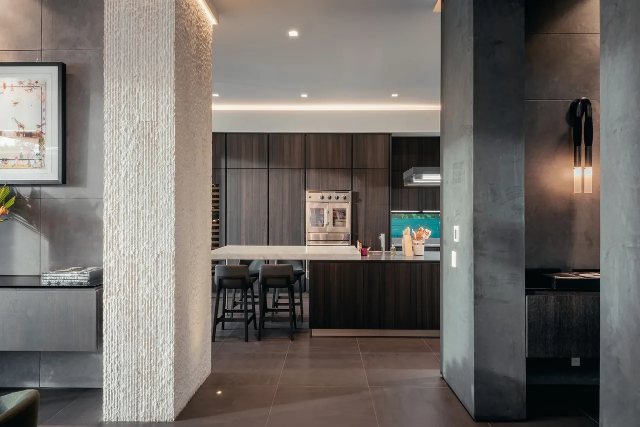 Modern kitchen features dark wood cabinetry, a kitchen island with stools, and textured wall details.