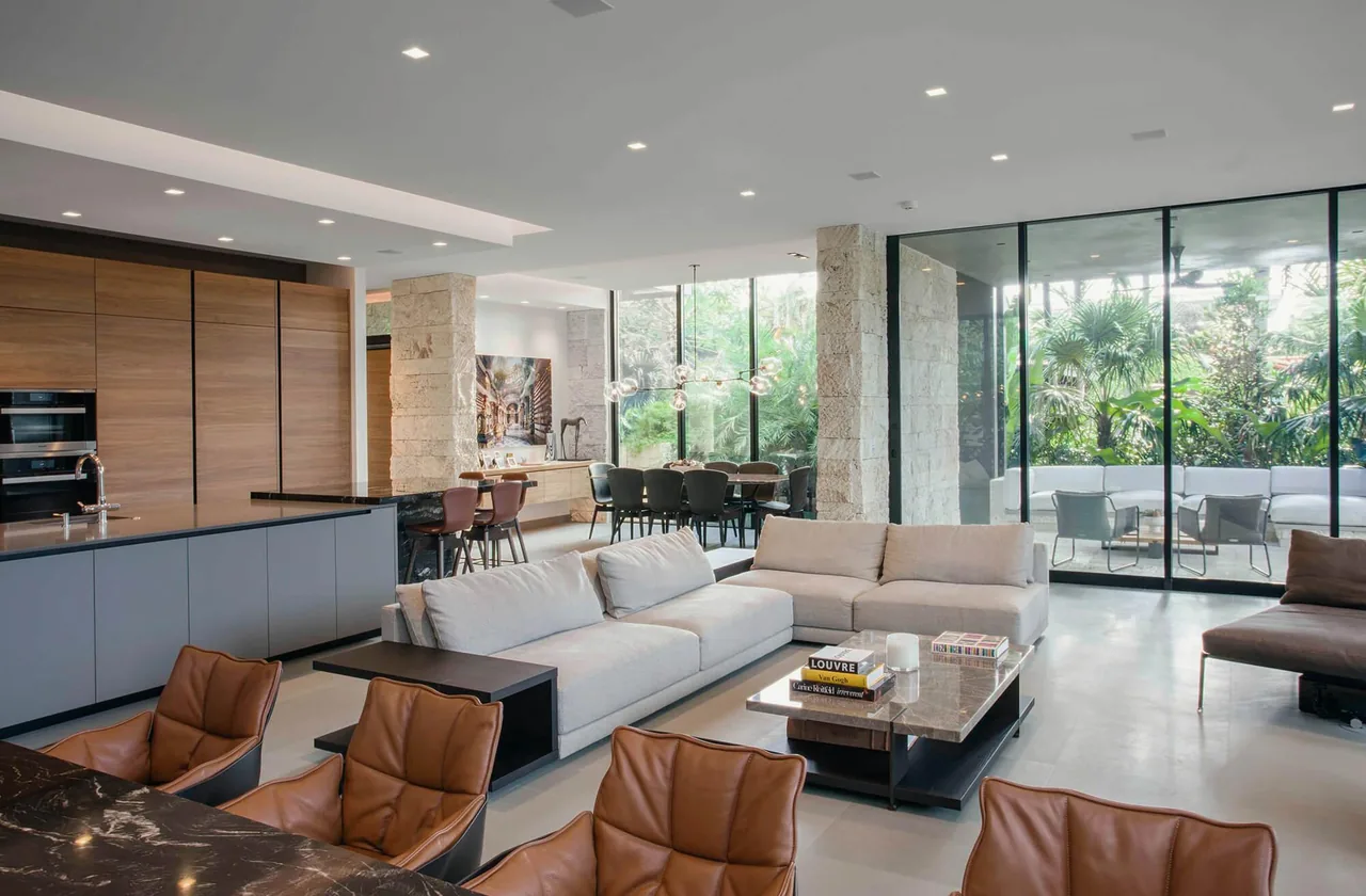 Living room and kitchen of the Janoura Residence feature floor-to-ceiling glass doors and natural stone columns.