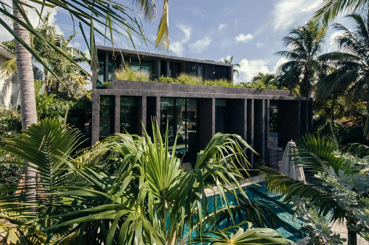 Janoura Residence features a modern, concrete facade with rooftop greenery and a pool, amidst lush tropical landscaping.
