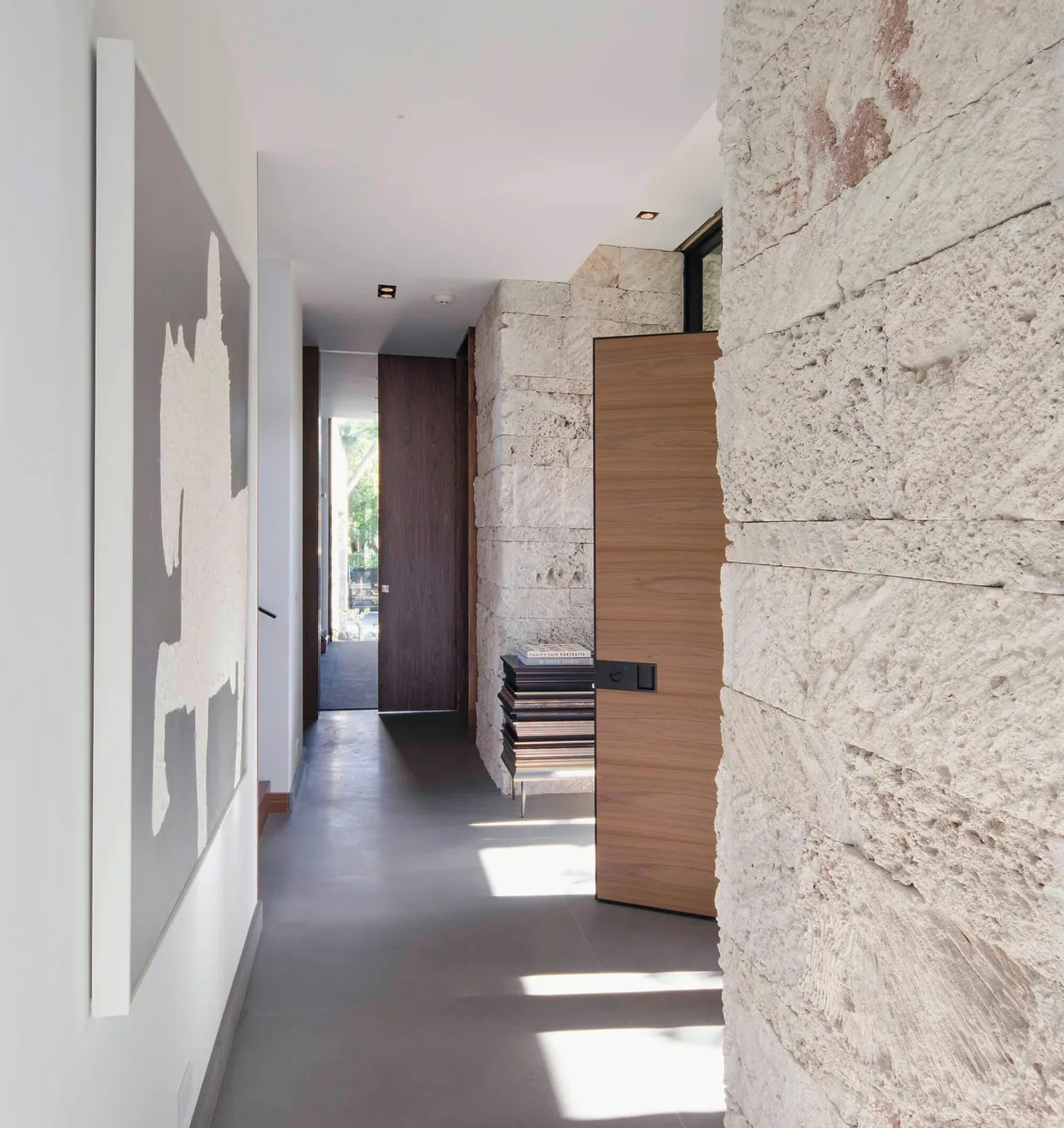 Hallway features textured natural stone wall with wood doors and minimal decor in Janoura Residence.