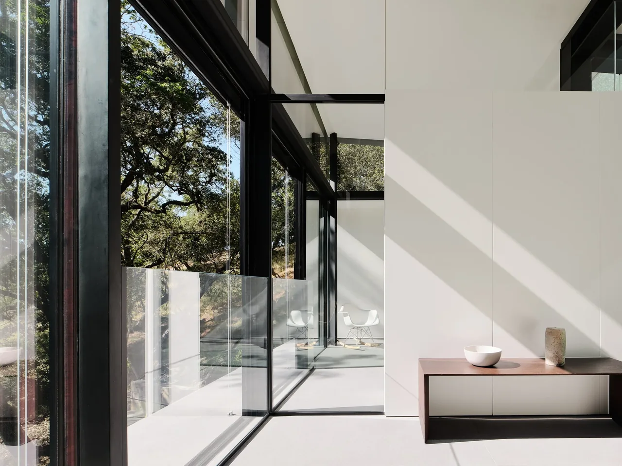 SUSPENSION HOUSE features floor-to-ceiling glazing and a minimalist interior with glass railing overlooking the wooded hillside.