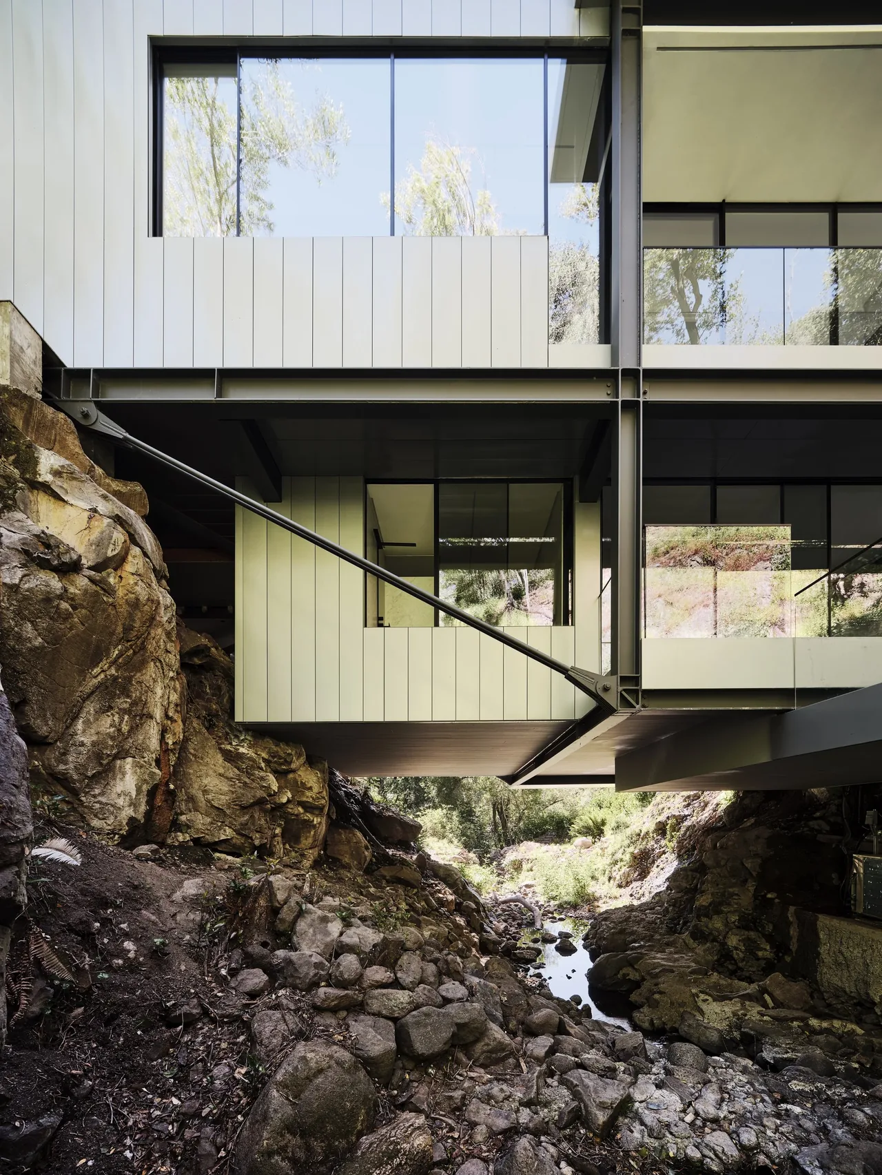 The Suspension House features a multi-level design with black steel framing and floor-to-ceiling windows overlooking rocky ground below.