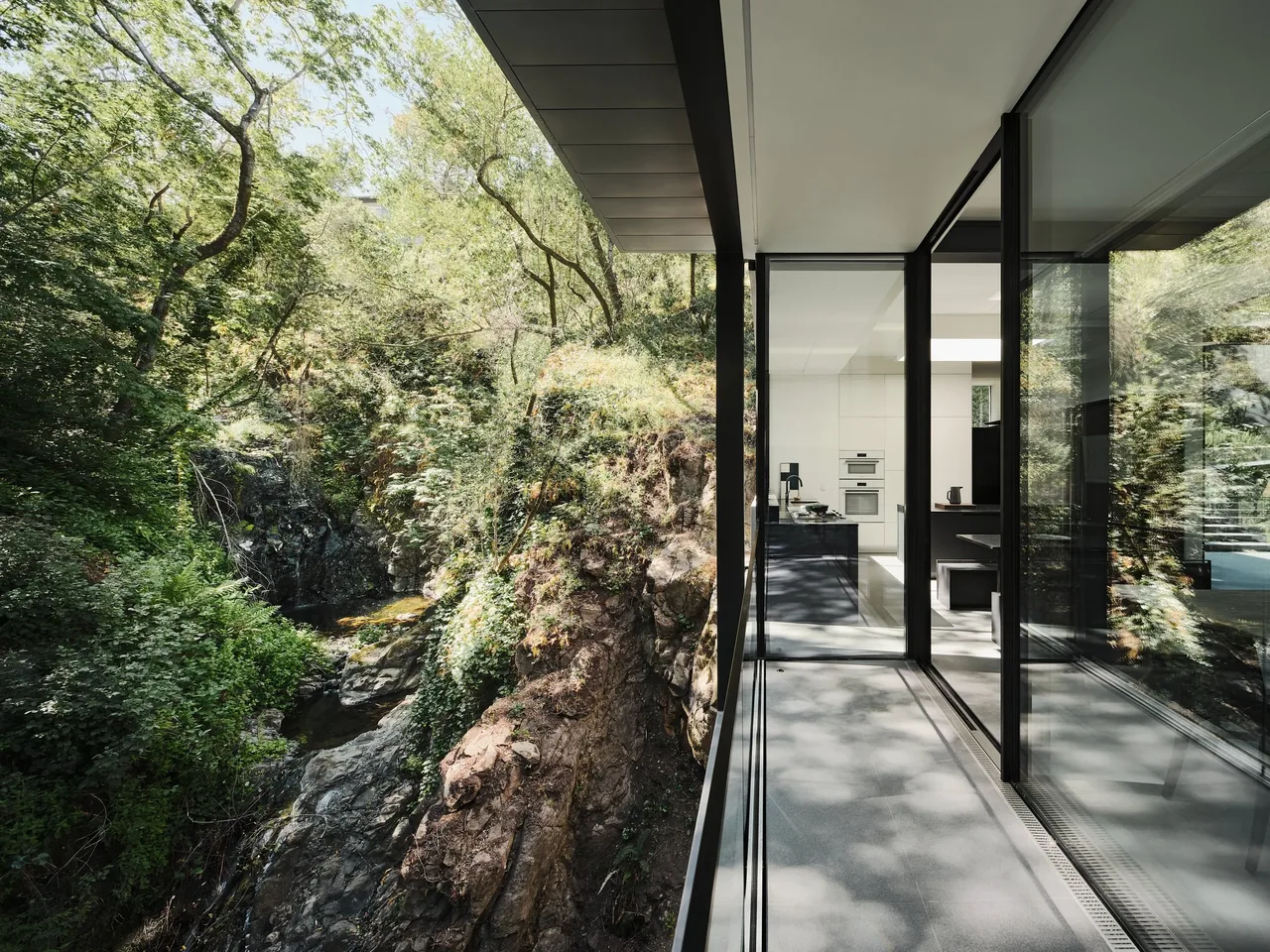 Balcony with glass sliding doors overlooks a wooded rocky hillside at Suspension House by Fougeron Architecture.