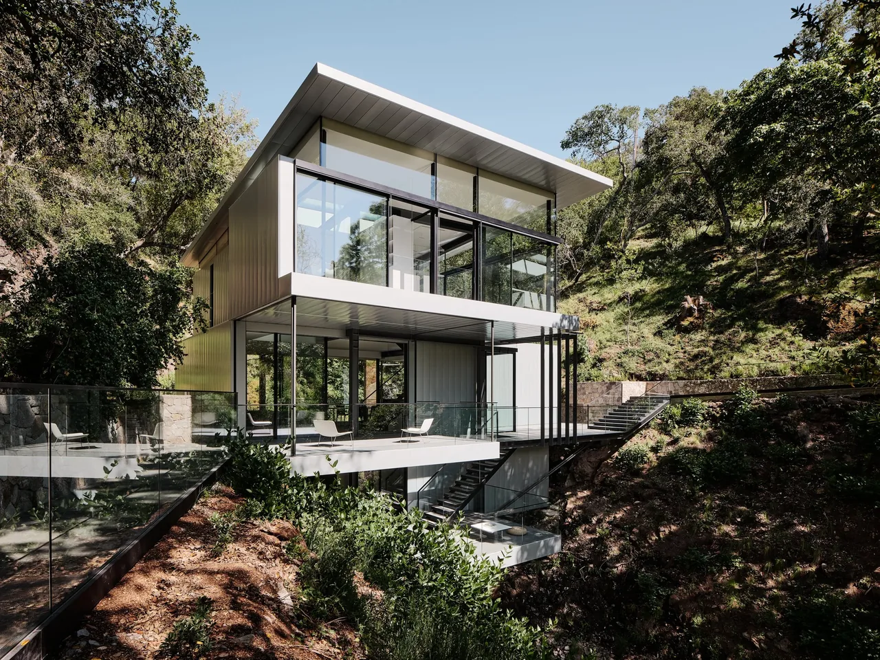 The Suspension House features a minimalist modern design with extensive glass and blackened steel on a steep site.