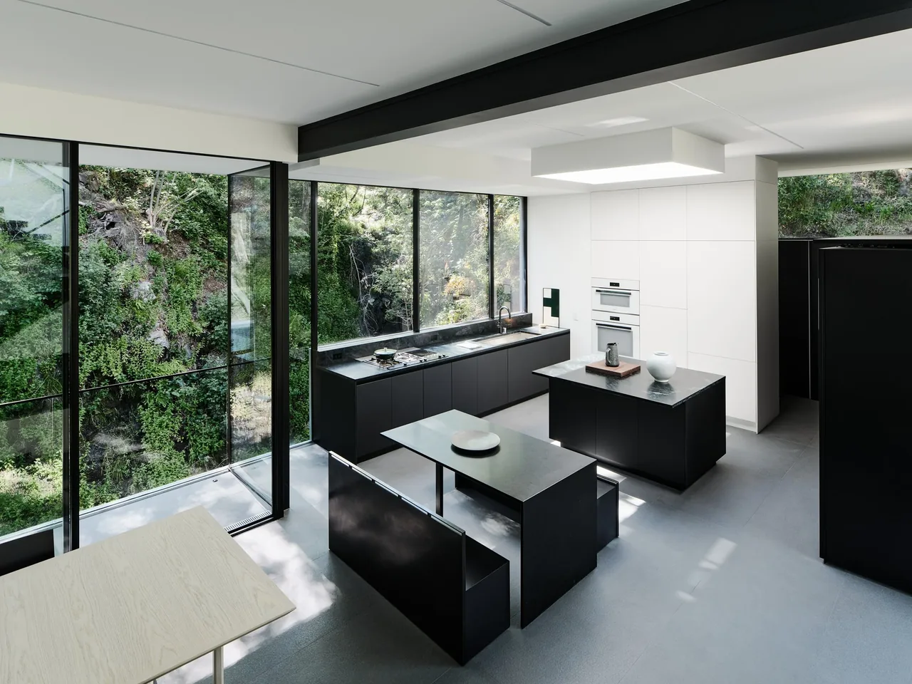 The kitchen of Suspension House features minimalist black cabinetry and expansive glazing that frames the wooded hillside outside.