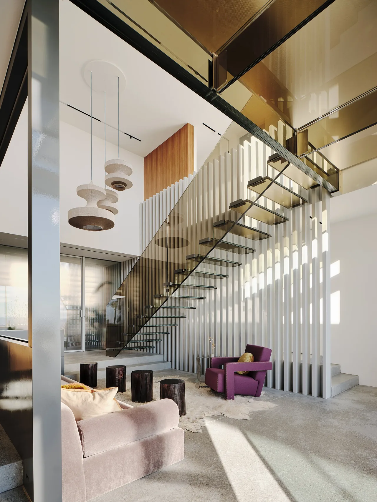Living space featuring a floating glass staircase and vertical white wood slat screen.