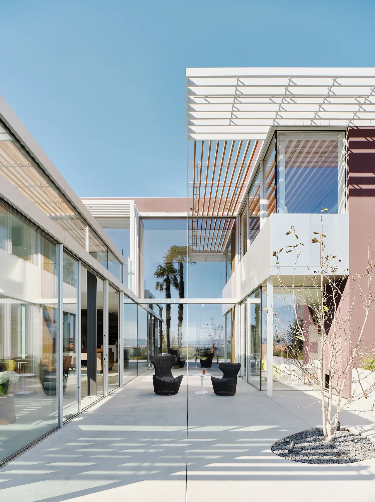 Glass-walled courtyard with outdoor chairs beneath a white pergola roof at the Translucence project in San Francisco.