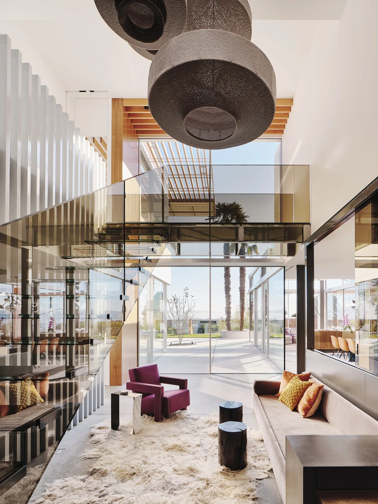 Living room features a glass staircase, large woven pendant lights, and floor-to-ceiling windows opening to a courtyard.