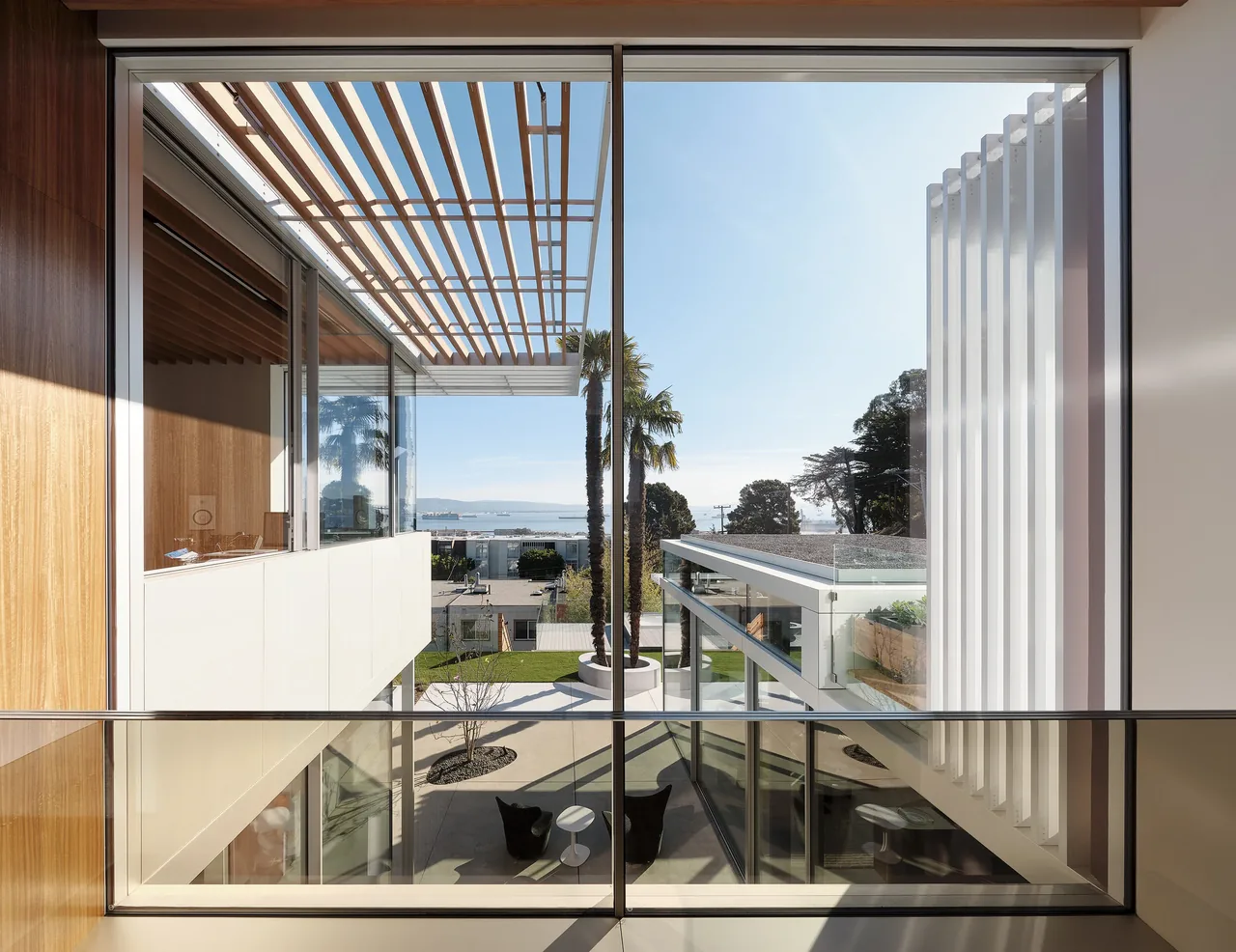 View of the courtyard with palm trees and modern slatted roof structures at Translucence project.