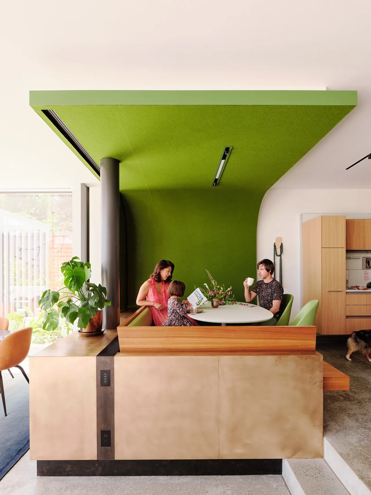 Dining nook features a green curved ceiling element with wood bench seating and a round white table.