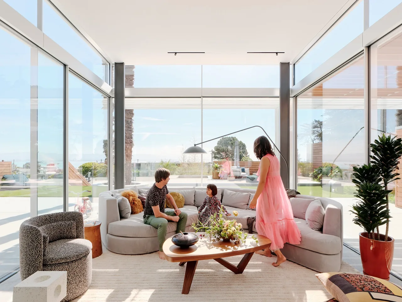 Living room in the Translucence project with floor-to-ceiling glazing and a curved sofa centered around a wooden coffee table.