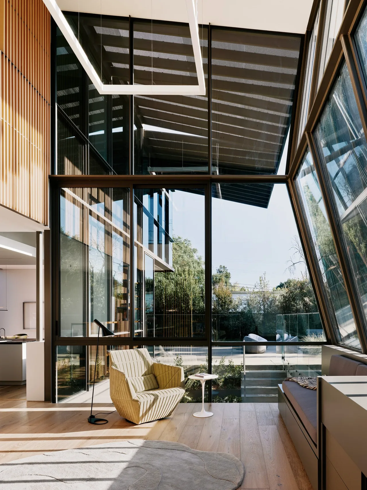 Modern living area features floor-to-ceiling corner windows with angled glass and light wood flooring.