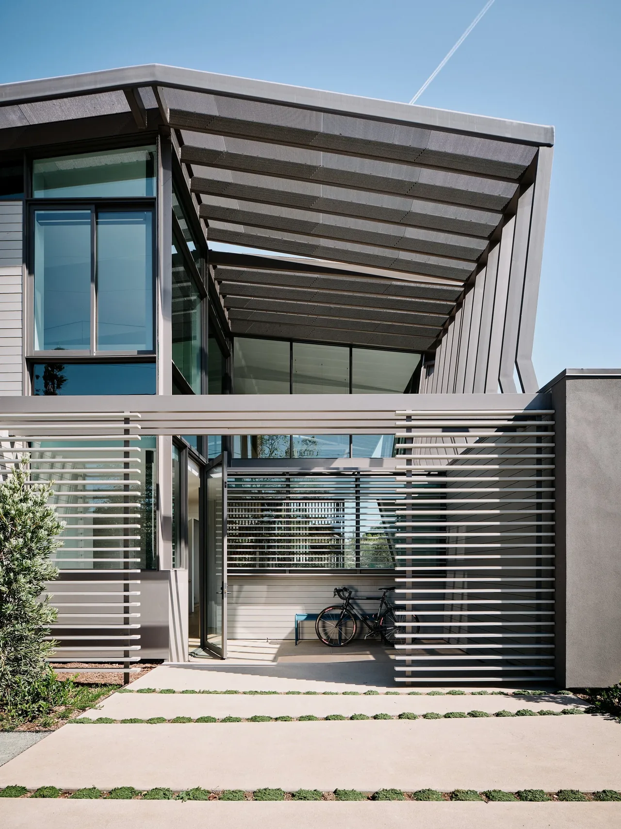 WAVELET features a contemporary metal mesh pergola, horizontal slat fencing, and large corner windows that allow natural light into the home.