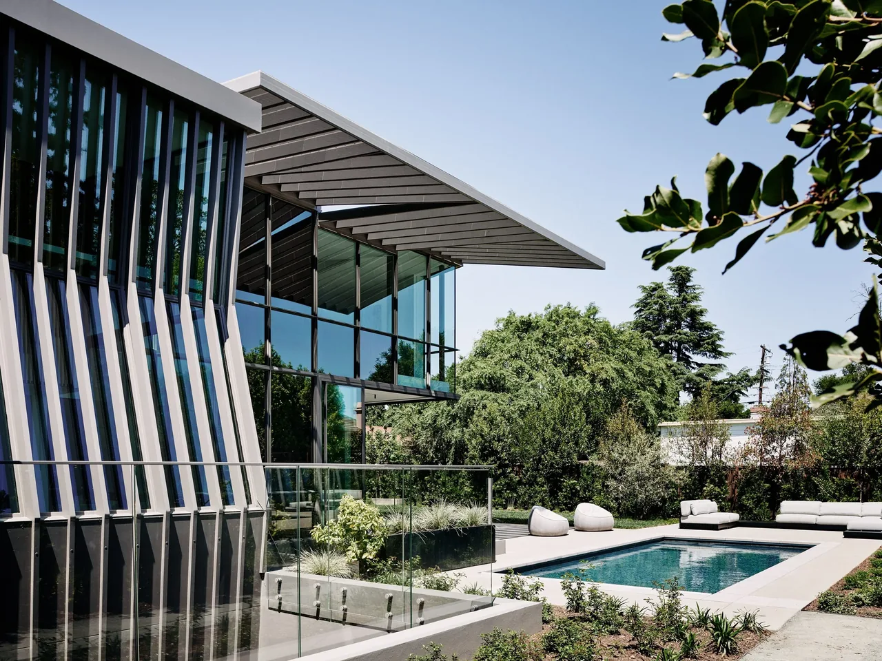 Modern residential exterior features angled vertical windows and a rectangular pool with outdoor seating.