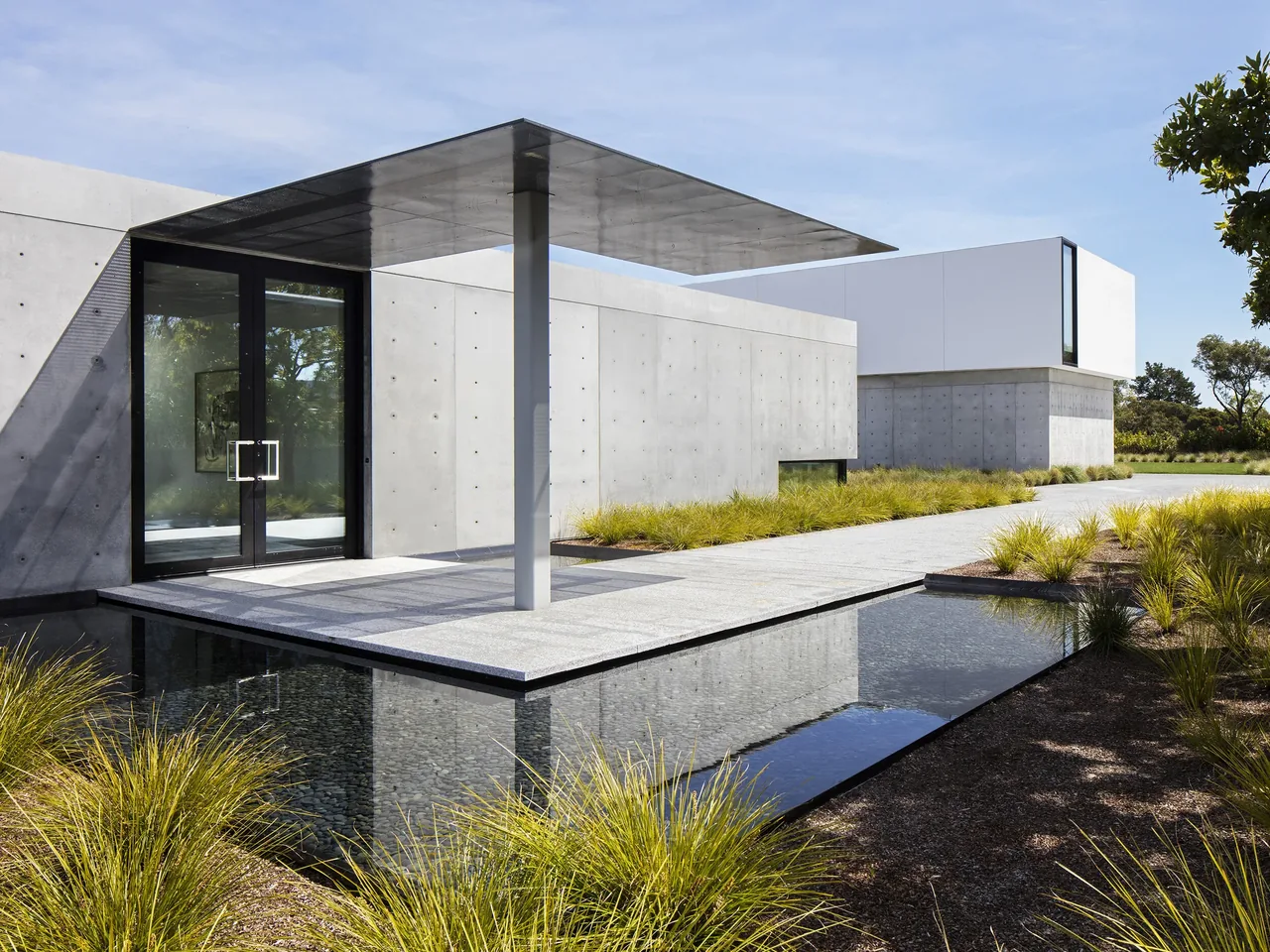 OZ Residence features a concrete exterior wall, metal canopy, and a reflecting pool, integrating indoor and outdoor spaces.