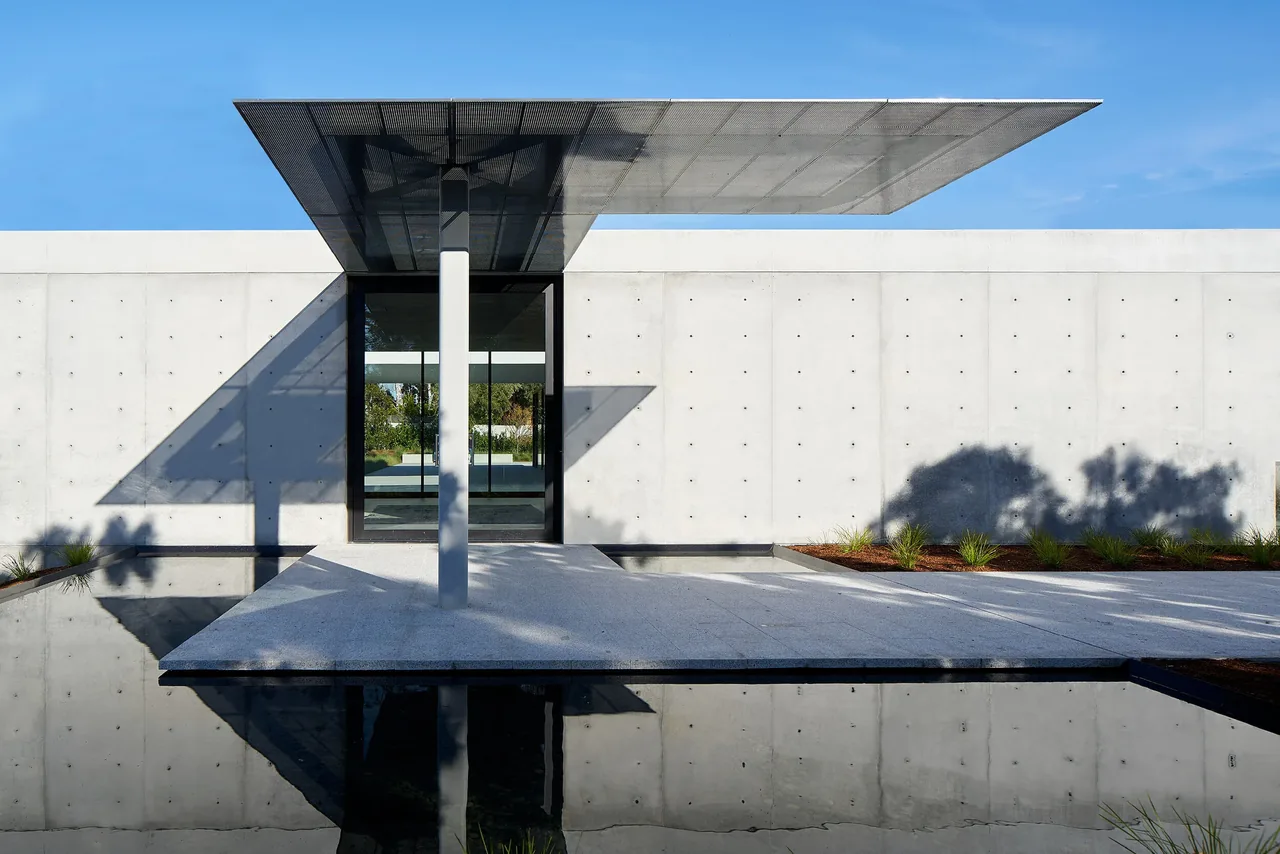 The OZ Residence features a concrete exterior with a cantilevered metal canopy over the entrance and a reflecting pool.