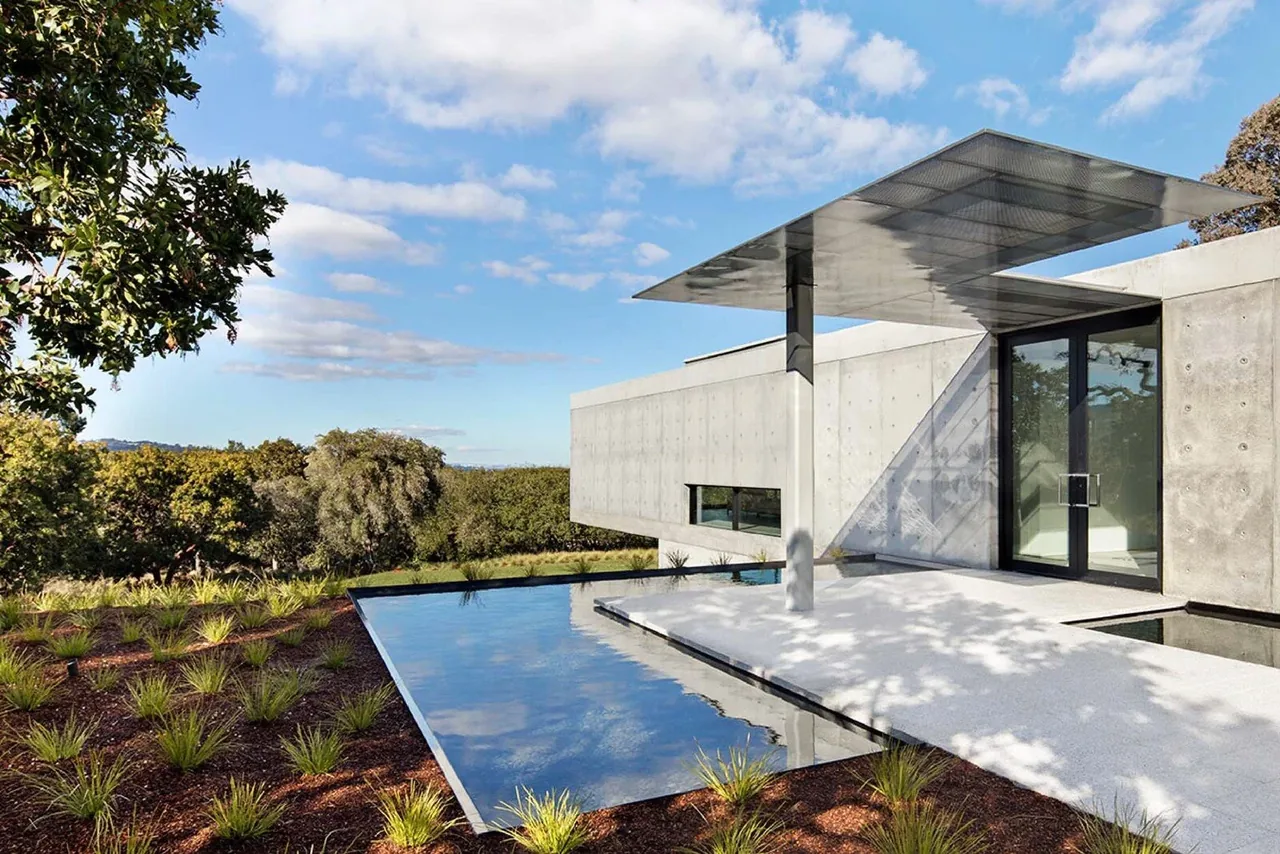 OZ Residence features a cantilevered concrete volume over a reflecting pool with a metal canopy at the entry, surrounded by landscaped grounds.