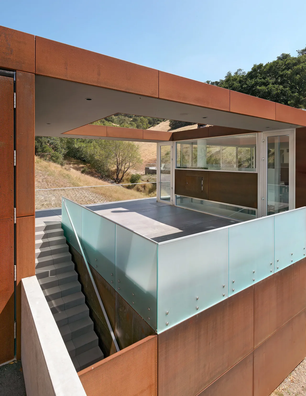Modern steel-framed building exterior with frosted glass railings and a concrete staircase.