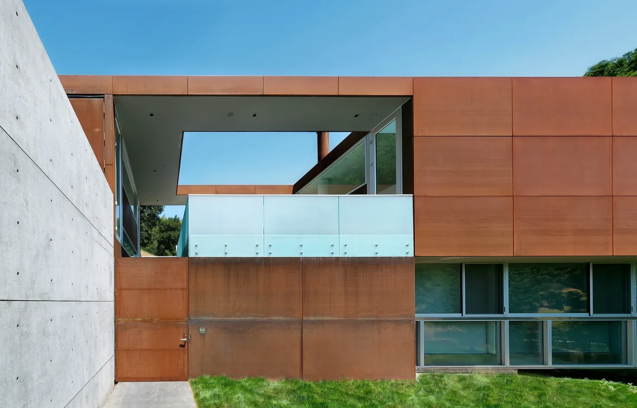 Front exterior of a modern steel and concrete house featuring flat roof and corner window details.