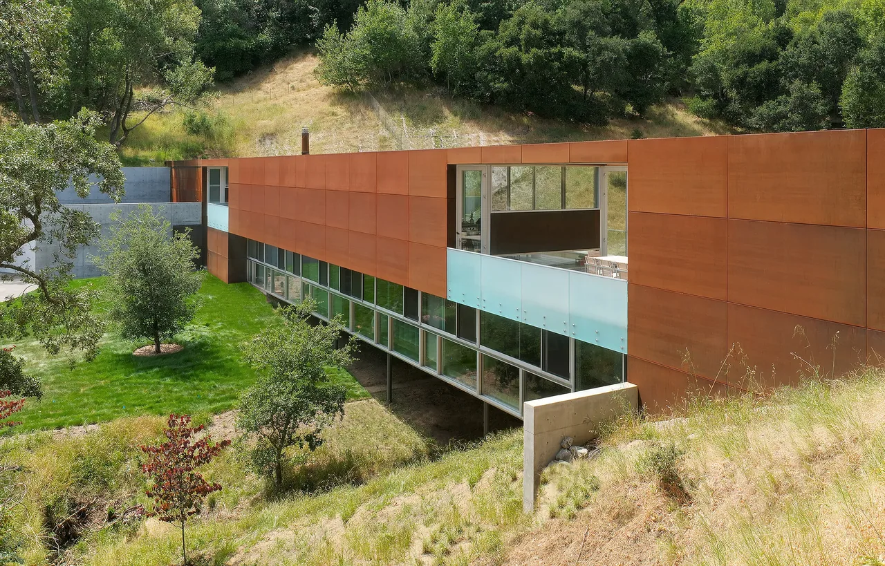 Front exterior view of Bridge House showing steel and concrete cladding with extensive glazing and landscape integration.