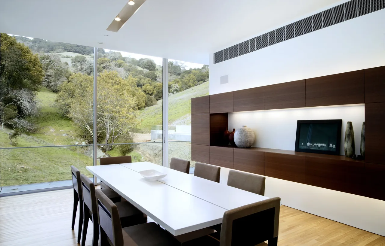 Dining room featuring floor-to-ceiling glazing with views of surrounding greenery and integrated wall cabinetry.