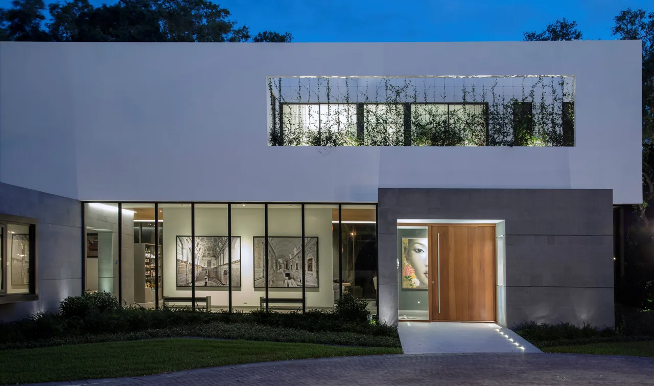 Two-story modern residence exterior featuring large glass walls, flat roof, and integrated courtyard planting.