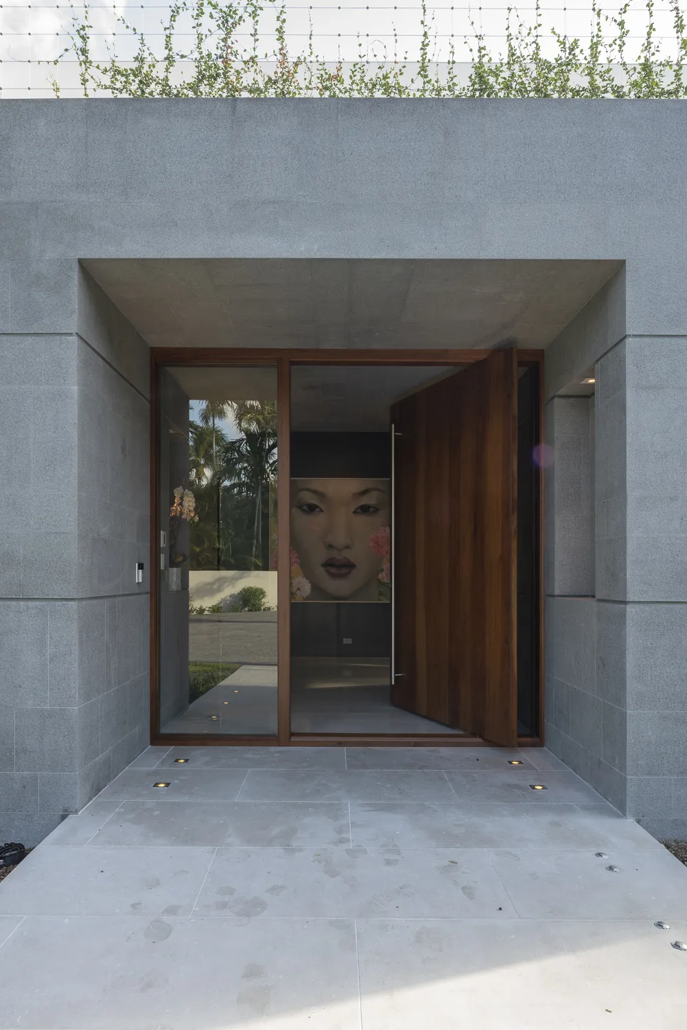 Entrance of a modern residence featuring gray stone cladding and a large wooden pivot door.