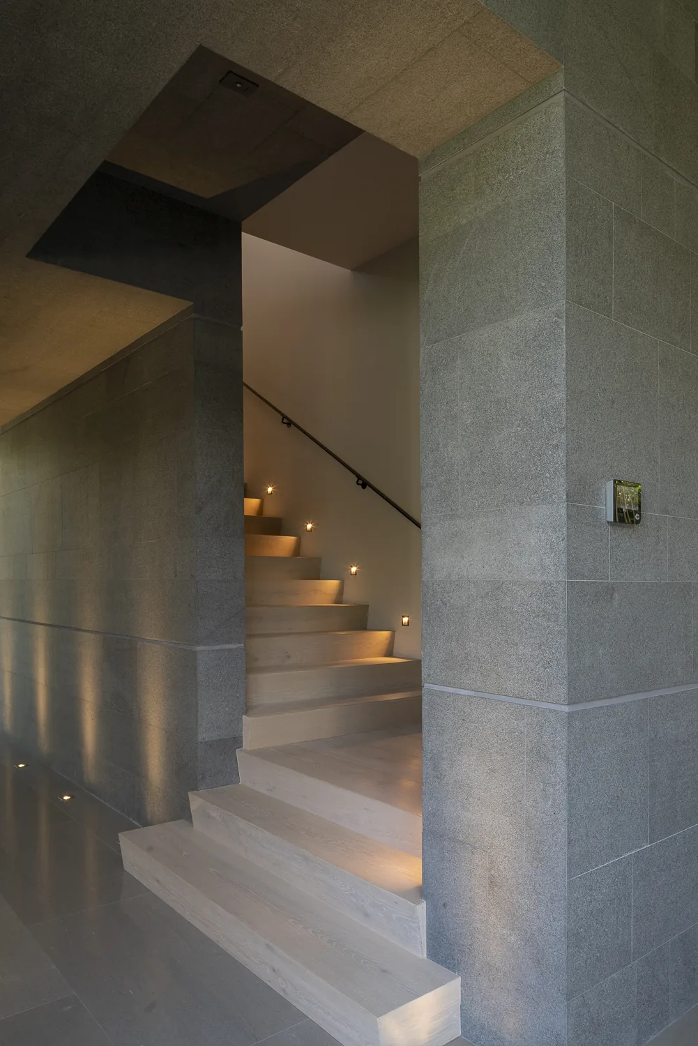 Wooden stairway with built-in step lights along a stone wall in the stairwell.