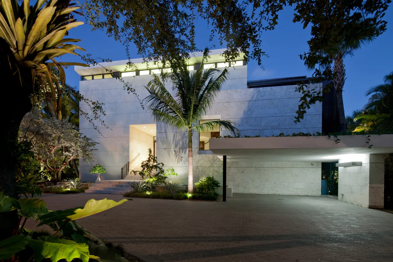 Coral Gables Residence by Touzet Studio shows a modern white stone exterior with flat roof and tropical palm trees at dusk.