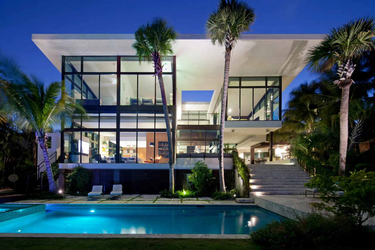 The Coral Gables Residence by Touzet Studio features floor-to-ceiling glazing and a flat roof with tropical landscaping and a swimming pool.