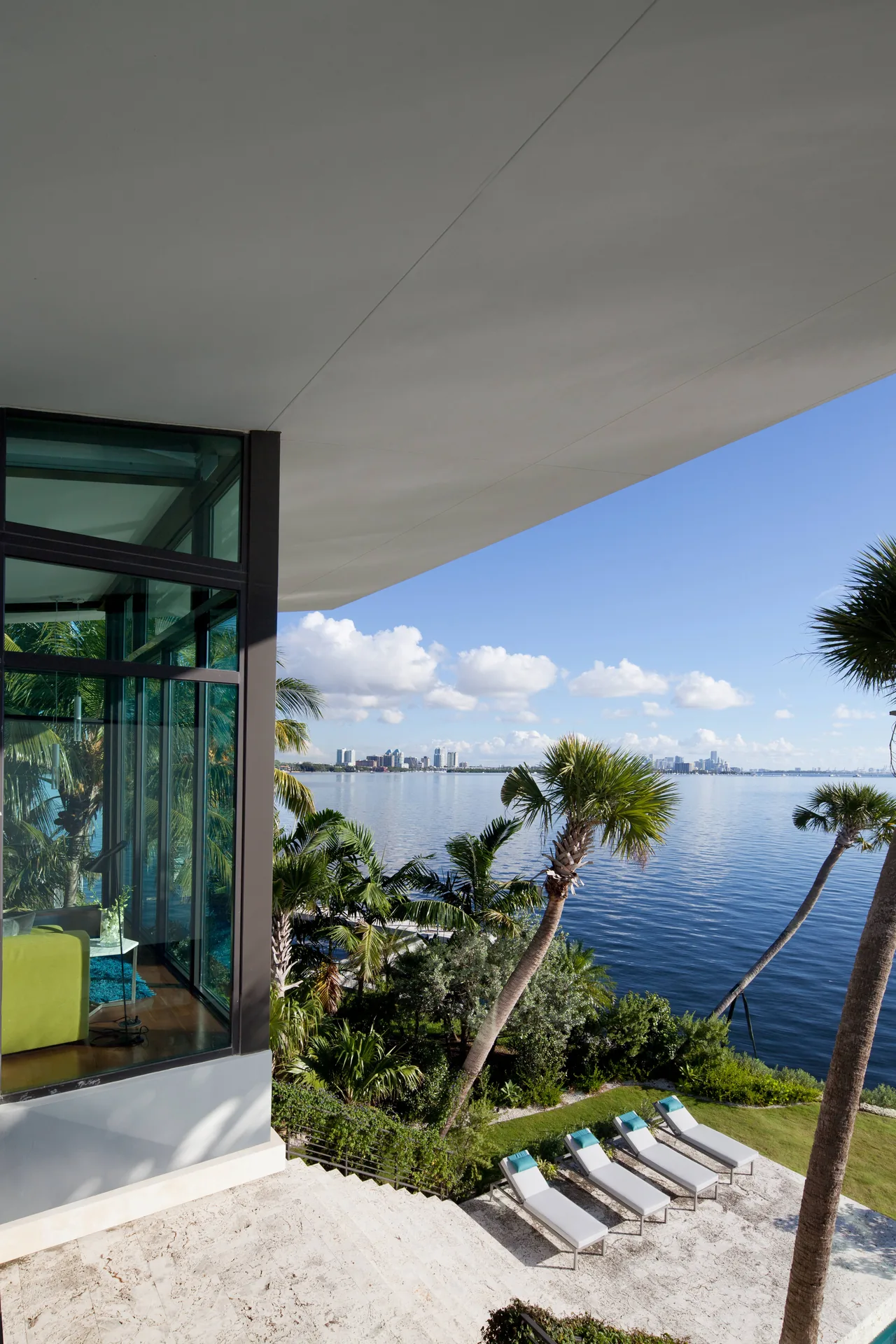 Waterfront terrace with tropical landscaping and lounge chairs at Coral Gables Residence in Miami.