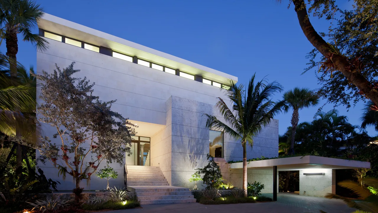 Modern residence features flat roof, clerestory windows, and tropical landscaping with palm trees and a carport.
