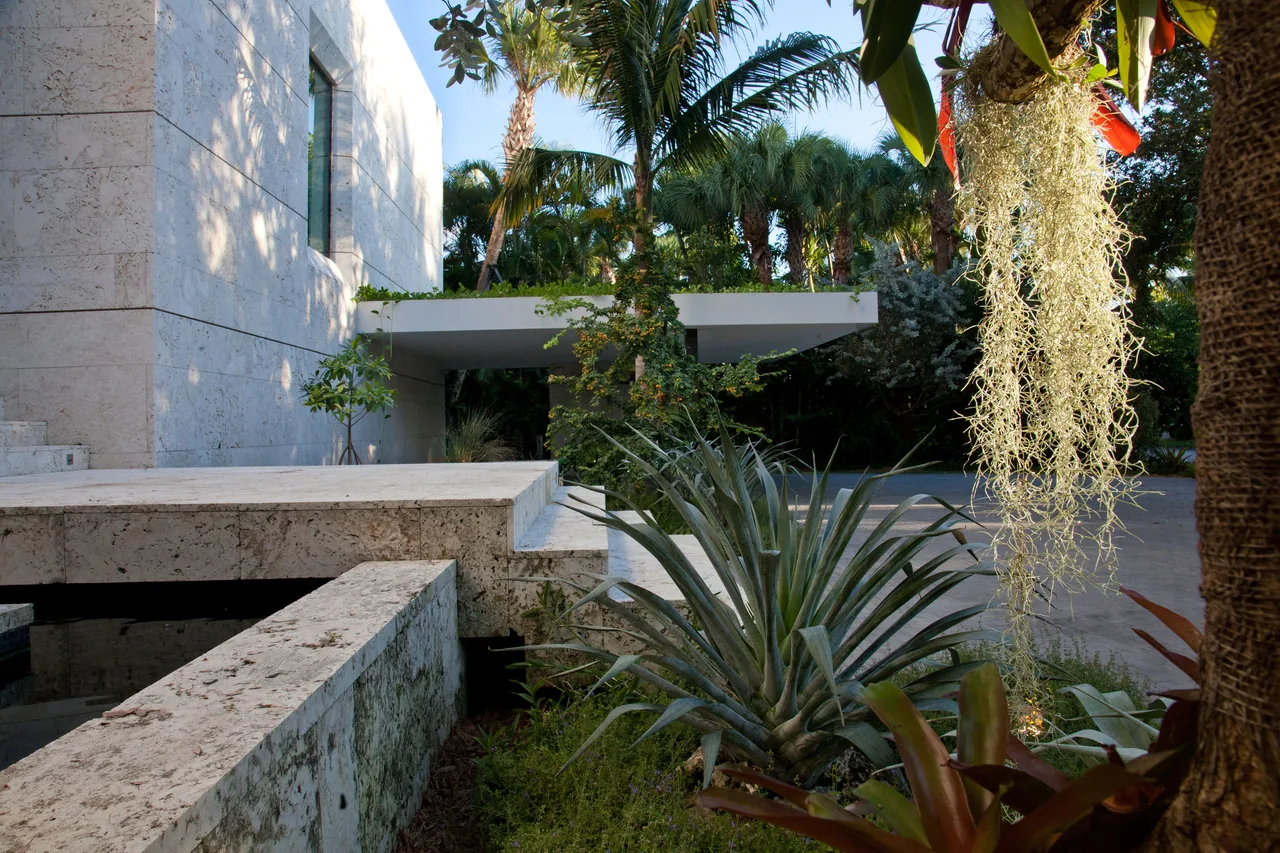 The Coral Gables Residence features stone walls and a covered patio surrounded by tropical landscaping.