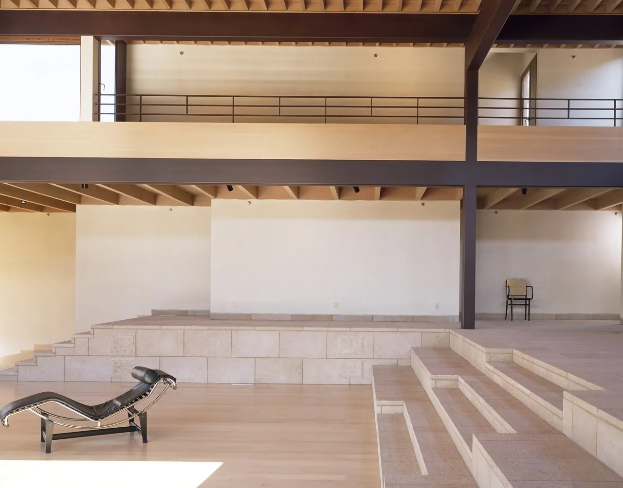 Multi-level interior space with tiered stone steps, wood ceiling panels, and metal structural beams at Di Napoli Residence.