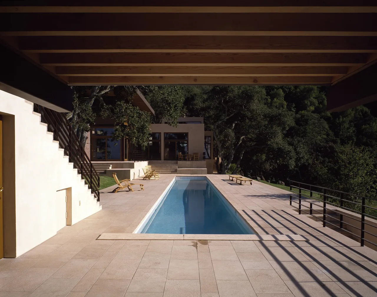 Pool terrace at Di Napoli Residence features stone tile flooring, metal railings, and outdoor seating with an overhanging wood ceiling.