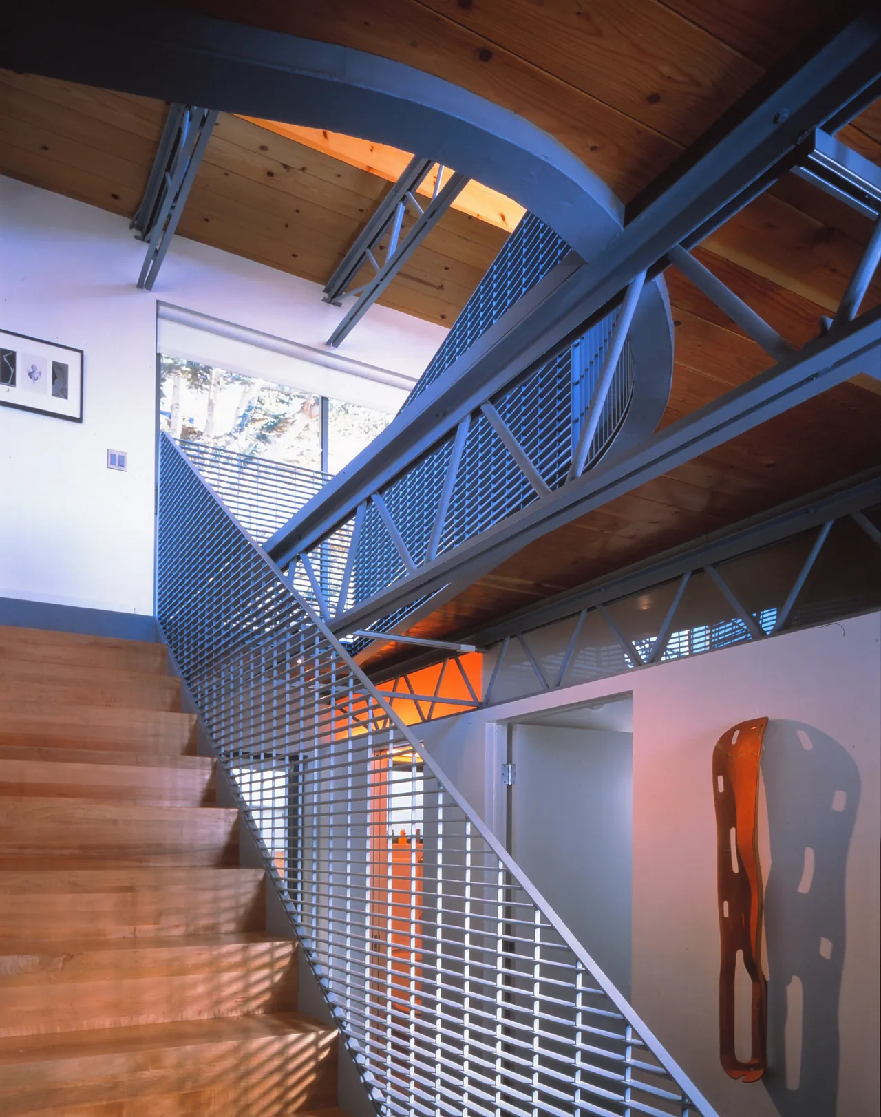 Interior view of a staircase featuring a curved wood ceiling and metal mesh railing with exposed ceiling trusses.