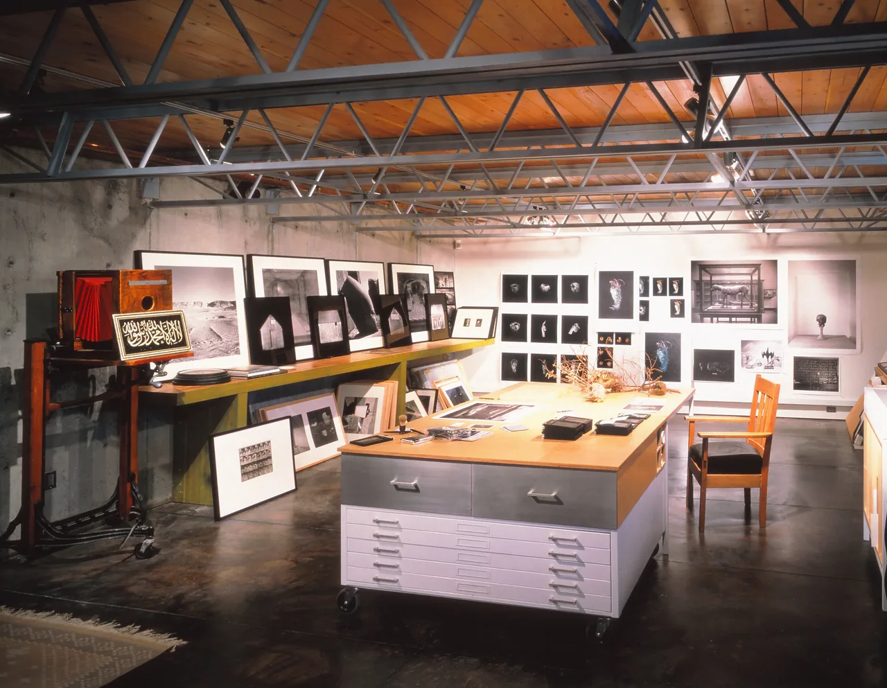 Barnes Residence interior workspace with photos and artwork displayed, highlighting an industrial metal truss ceiling and wood panels.