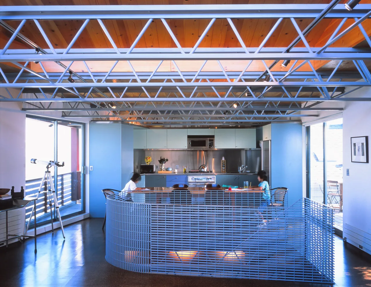 The Barnes Residence kitchen and dining area feature a curved metal mesh railing and exposed wood-beamed ceiling.