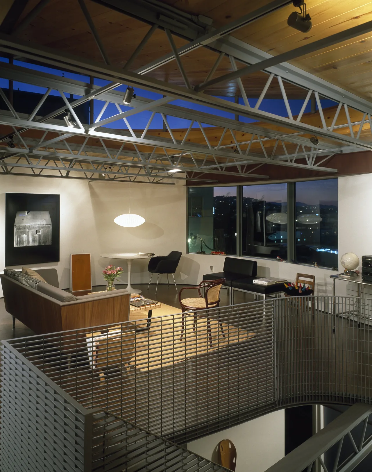 Living area in Barnes Residence features exposed metal trusses, large windows, and a mix of modern seating and wood accents.