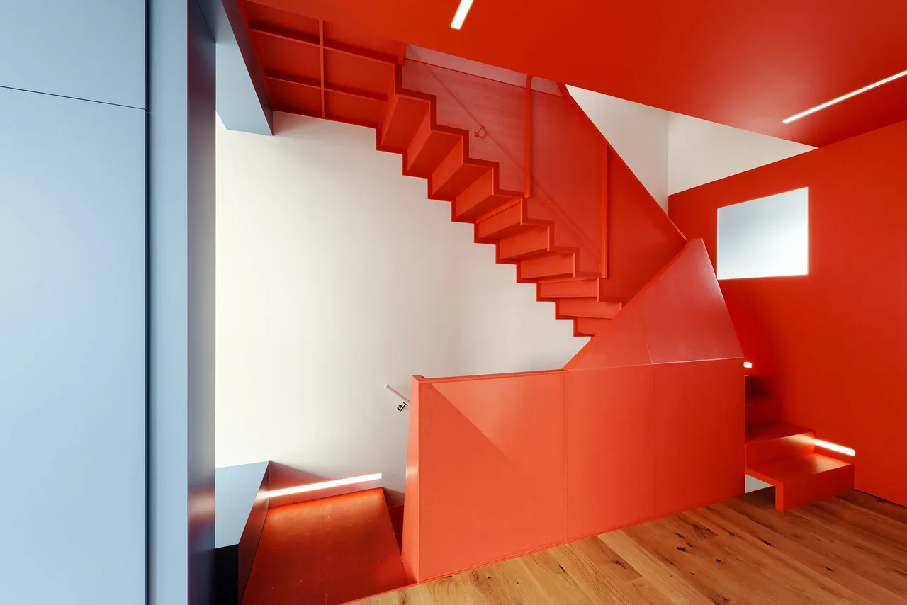 Modern staircase painted entirely in red with a square window and natural wood flooring in the space.