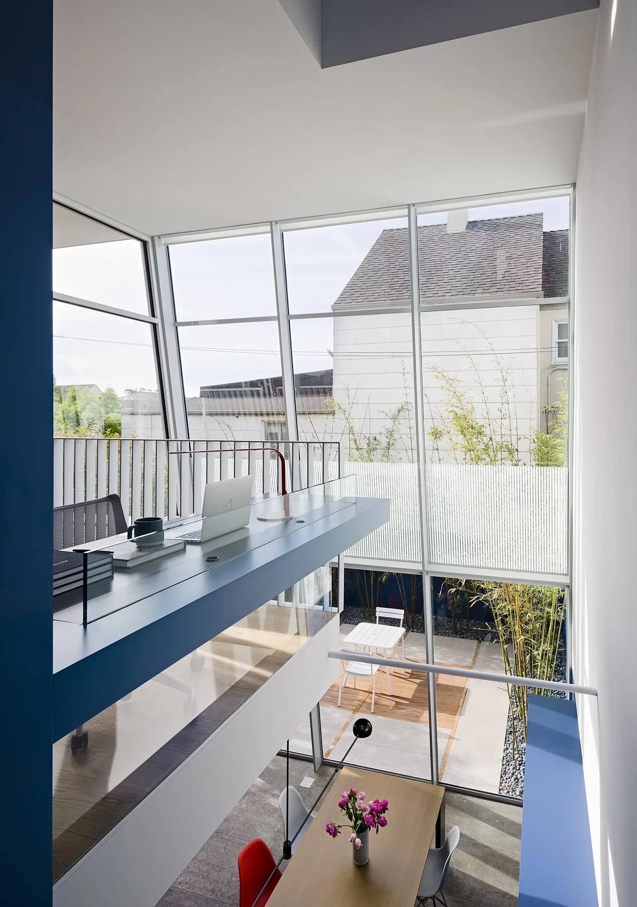 Modern two-story room features a blue floating desk and large windows opening to an outdoor seating area.
