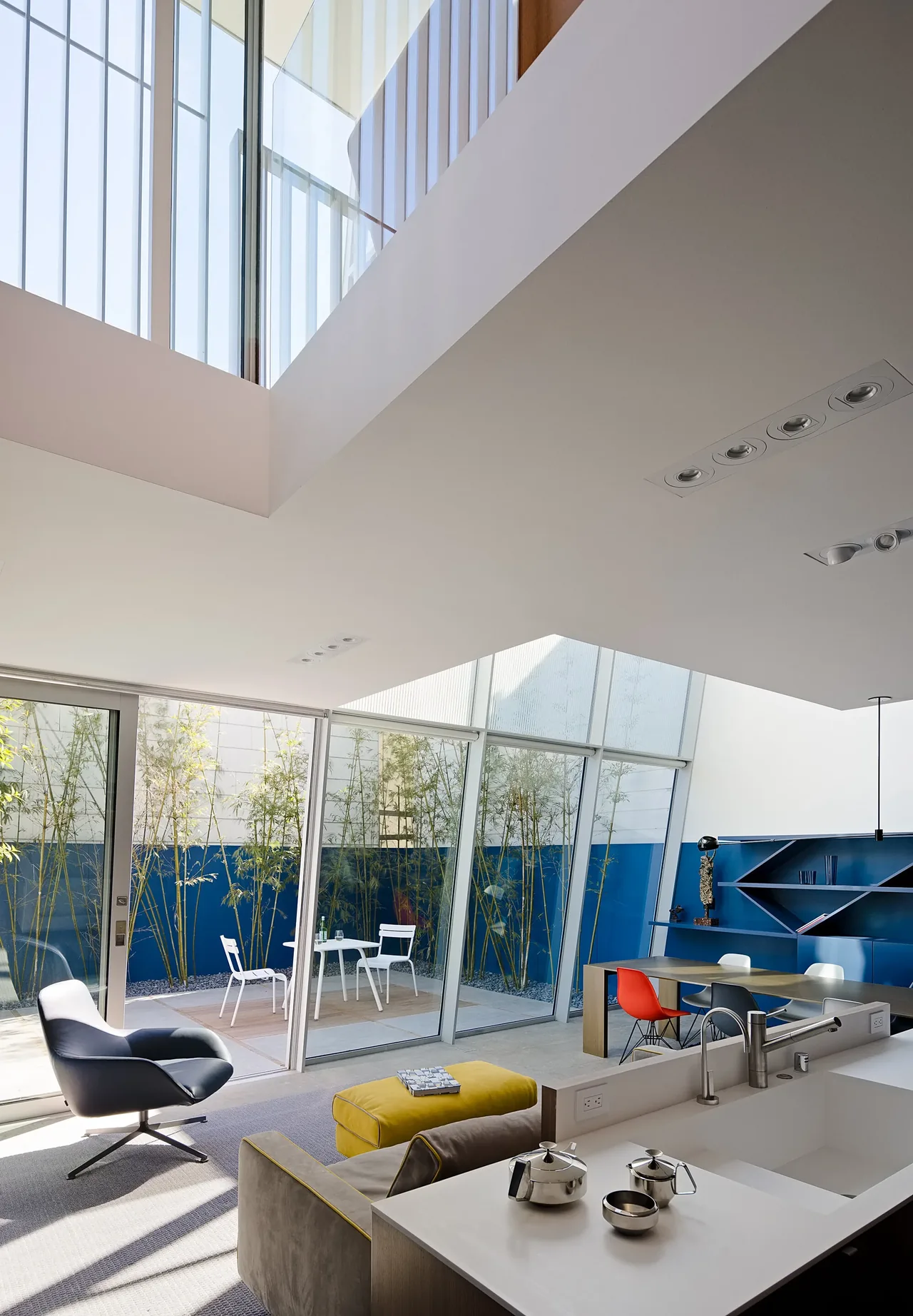Modern living area with large glass walls opens to a courtyard featuring bamboo and a small patio seating area.